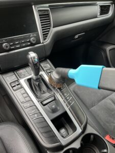 Odkurzanie konsoli środkowej samochodu miękką szczotką podłączoną przez adapter MojaSsawka