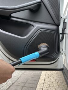Odkurzanie głośnika w drzwiach samochodu miękką szczotką podłączoną przez niebieski adapter MojaSsawka